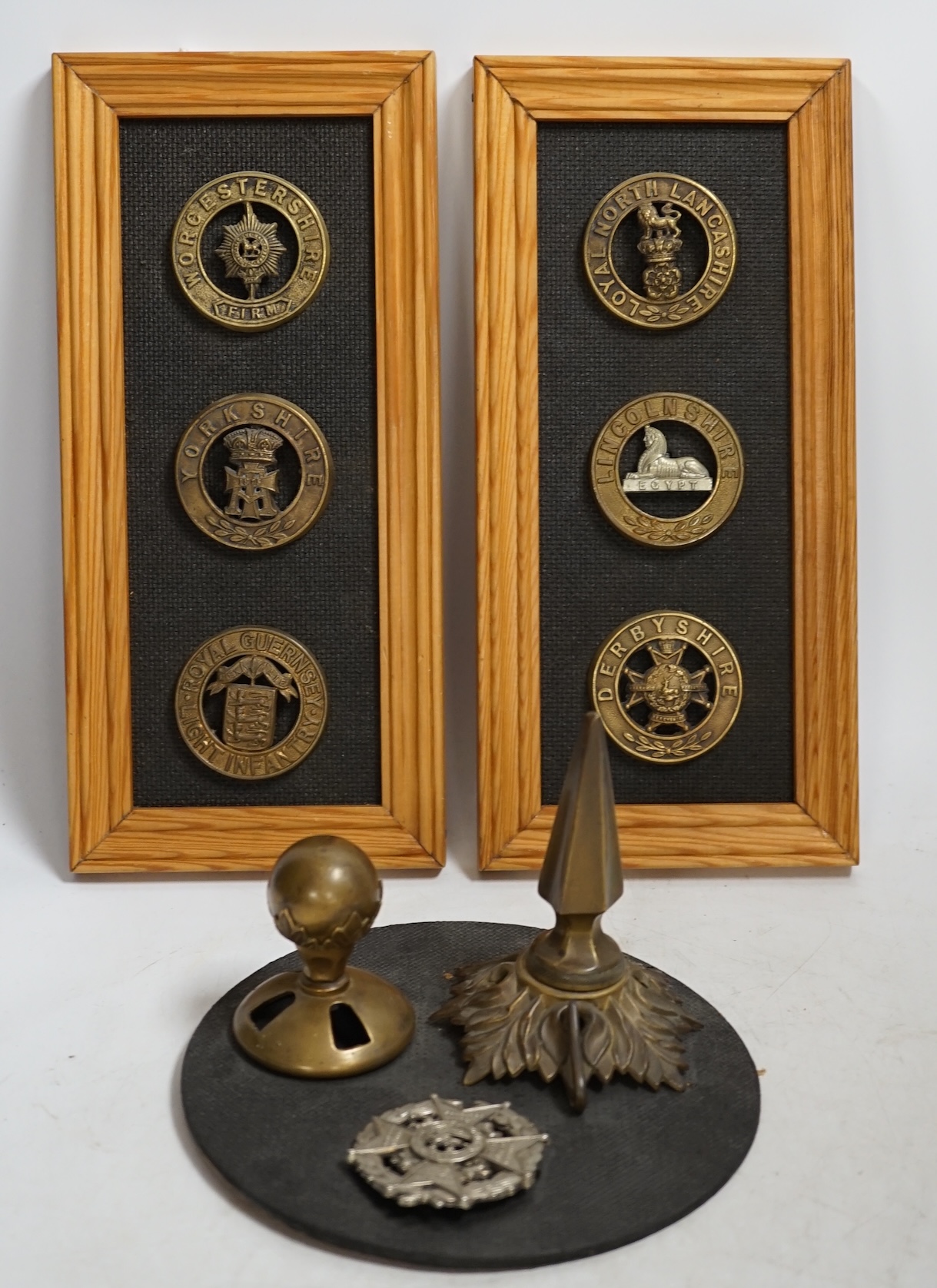 Six military helmet plates mounted on two boards, together with two helmet spikes and a cap badge, including; the Yorkshire Regiment, the Royal Guernsey Light Infantry, the Loyal North Lancashire, the Lincolnshire Regime